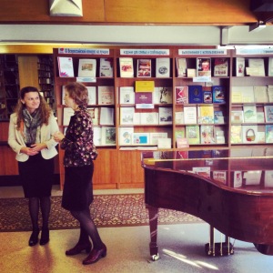 Two woman standing in front of a book shelf talking. 