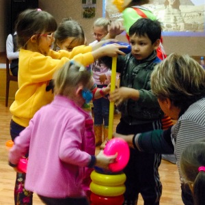 Four kids putting round objects on a stick, an activity that is symbolic of building. 